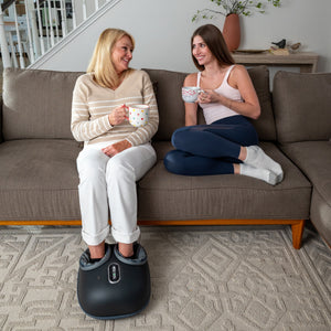 A Old Woman Use Foot Massager While Talking To A Young Woman On Sofa